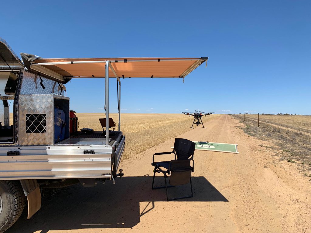 Sensorem drone coming to land next to a camper trailer on a farm.